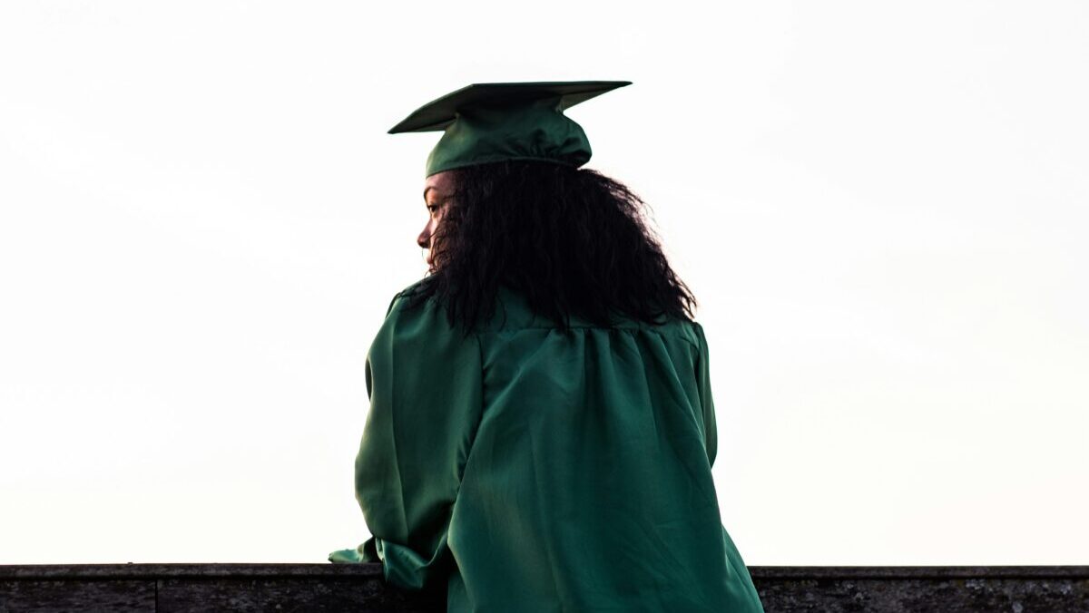 Girl standing in a green graduation cap and gown on graduation day